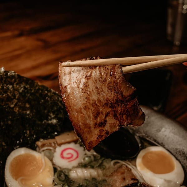 Chopsticks holding a piece of grilled pork belly over a bowl of Boru Ramen.
