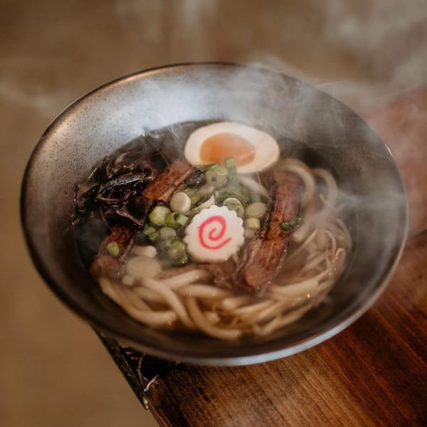 Steaming bowl of Boru Ramen with pork, egg, green onions, and narutomaki on a wooden table.