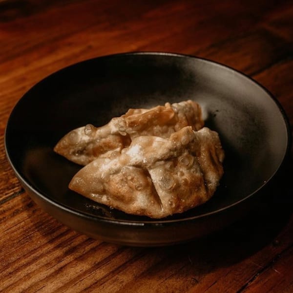 Two crispy Boru Ramen gyoza dumplings in a black bowl on a rustic wooden table.